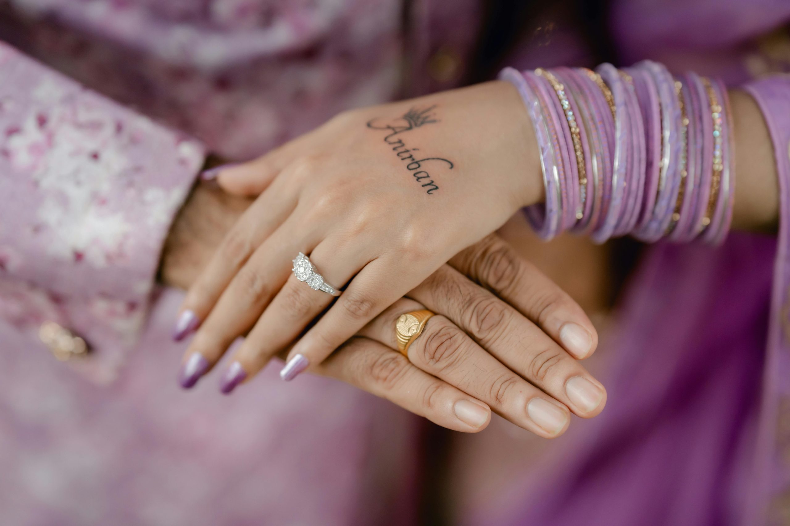 Close-up of hands showcasing wedding rings and lavender bangles, with henna tattoo. Perfect for wedding and jewelry themes.